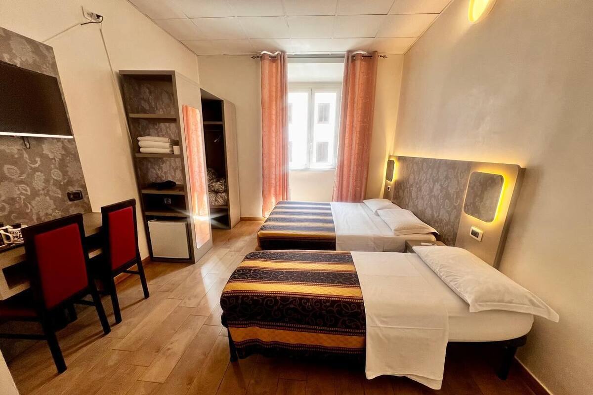 A hotel room with two beds, a desk, and a chair.