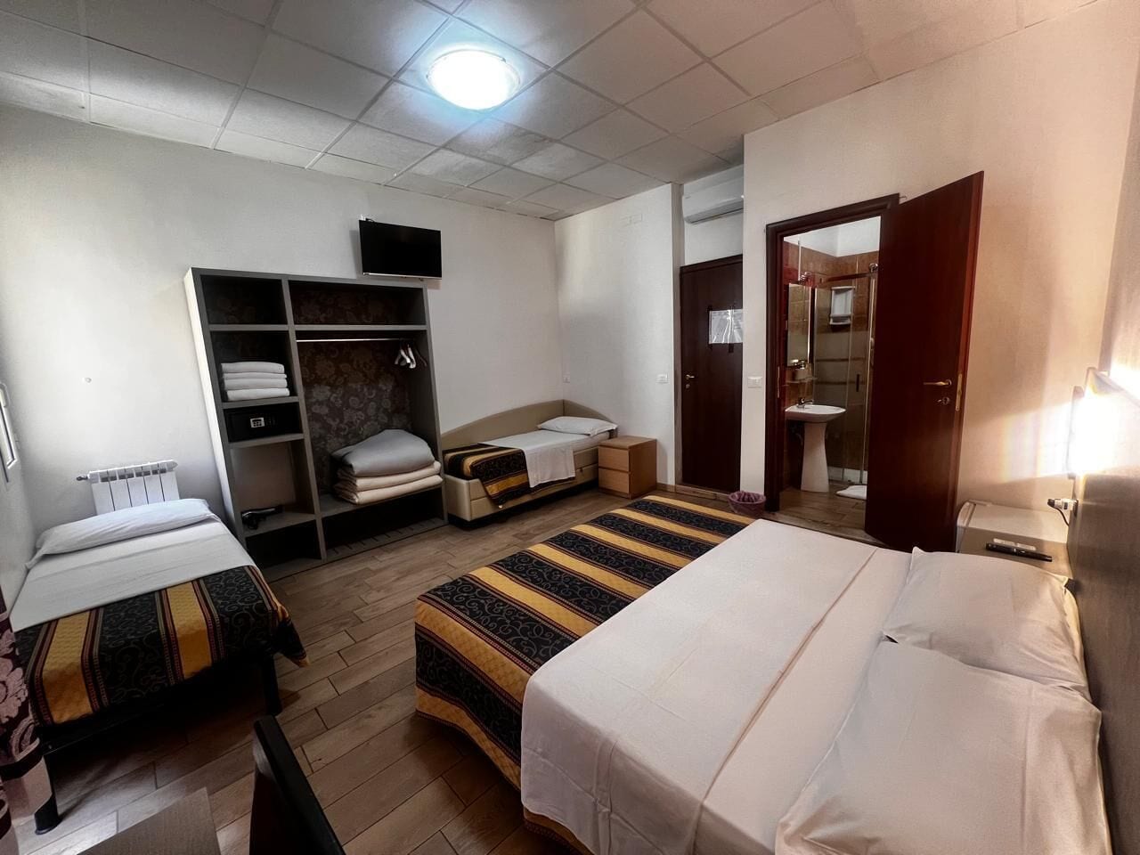 A hotel room with two beds, a wardrobe, a desk, and a bathroom.
