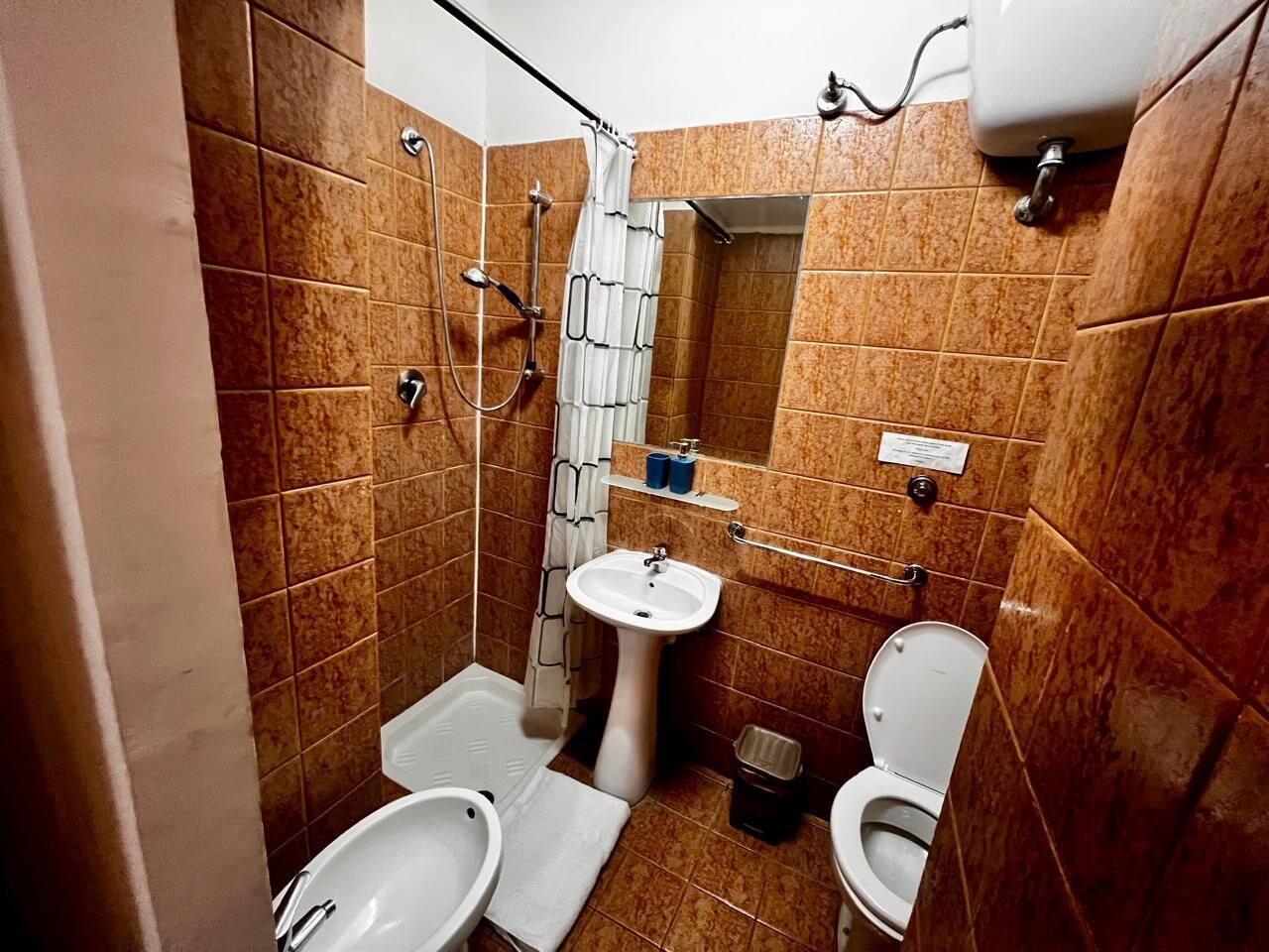 Un baño con ducha, dos inodoros, un lavabo y un espejo.