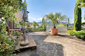 A patio with stone flooring, a wooden table, chairs, a large potted plant, and a palm tree. - Holiday Apartment "Jose" with Shared Pool, Terrace & Wi-Fi (Tremosine)