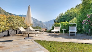 An outdoor patio with lounge chairs and a table, surrounded by greenery and mountains in the background. - Holiday Apartment "Jose" with Shared Pool, Terrace & Wi-Fi (Tremosine)