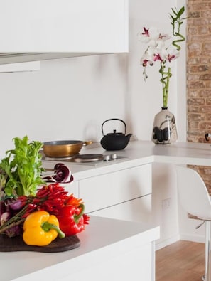A kitchen with a white countertop, a kettle, a bowl, and fresh vegetables.