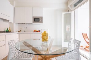 Una cocina moderna con armarios blancos, un microondas y una mesa de vidrio con sillas.