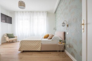 Une chambre à coucher comprenant un lit, une chaise, une table de chevet, une lampe fixée au mur et une porte.