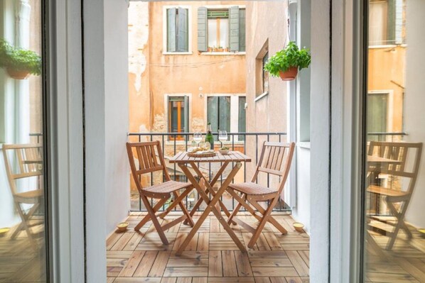 Un balcon avec une table et des chaises en bois, des plantes en pot et une vue sur les immeubles.