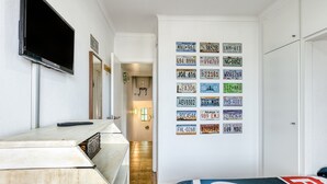 Ein Hotelzimmer mit einem Bett, einem an der Wand montierten Fernseher, einem Schreibtisch und einer Wand, die mit verschiedenen Kfz-Kennzeichen verziert ist.