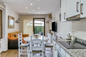 A compact kitchen with white cabinetry, a built-in stove, and a dining area with a round table and chairs. - Holiday Home "Set Cases" with Sea View, Shared Pool & A/C (L'Escala)