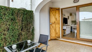 Eine Terrasse mit Glastisch und -stühlen, einer Holztür und Blick in einen Küchenbereich.