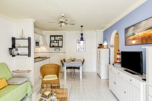 A living room with a sofa, a dining table, a TV, and a ceiling fan. - Holiday Apartment "Els Pins" with Shared Pool, Balcony & Wi-Fi (L'Escala)