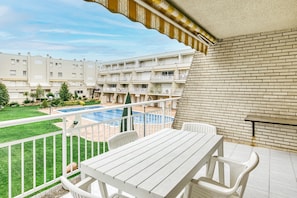 A balcony with a pool, white furniture, and a view of a multi-story building with balconies.