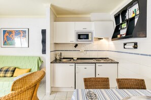 A compact kitchen with a microwave, a sink, and a small refrigerator. There is a dining area with a table and chairs. - Holiday Apartment "Els Pins" with Shared Pool, Balcony & Wi-Fi (L'Escala)