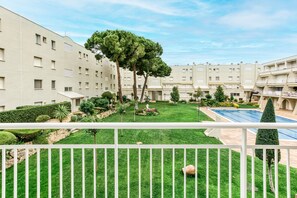 A courtyard with a swimming pool, green lawns, and a white fence.