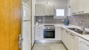 A modern kitchen with white cabinets, a built-in oven, a coffee maker, and a sink.