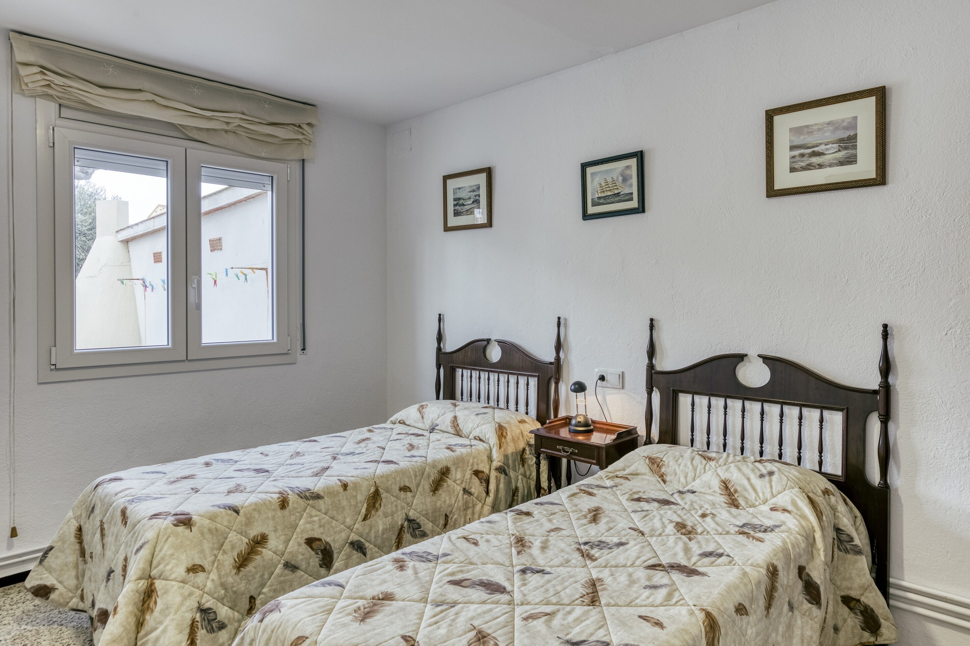 A bedroom with two beds, a window, and three framed pictures on the wall.