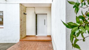 A narrow outdoor corridor with a white door, a brick wall, and a tiled floor.