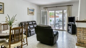 A living room with a sofa, TV, fireplace, dining table, chairs, and a sliding glass door leading to an outdoor area.