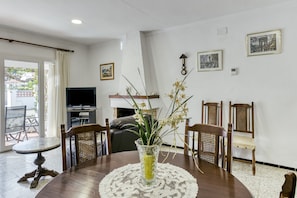 Un coin repas avec une table ronde, des chaises, un vase de fleurs, un téléviseur et des tableaux encadrés au mur.