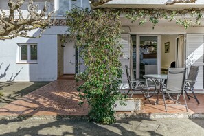 A patio with a table and chairs, a white building, and a tree with green leaves.
