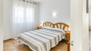 A bedroom with a bed, curtains, a nightstand with a lamp, and a wall-mounted light. - Holiday Home 'Allegra' with Private Pool, Wi-Fi and Air Conditioning (L'Escala)