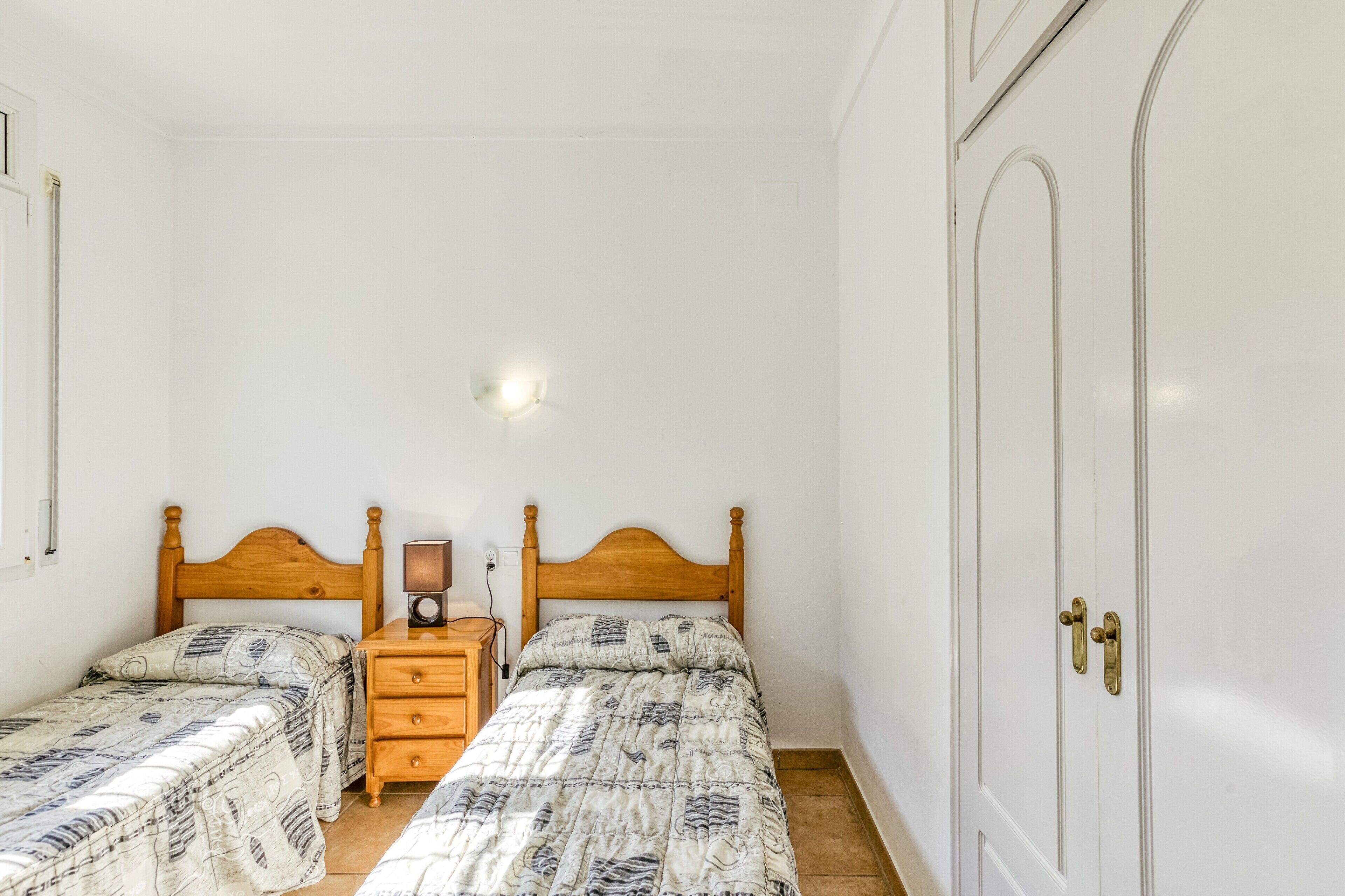 Una camera da letto con due letti singoli, un comodino con una lampada, un armadio e un punto luce a parete.