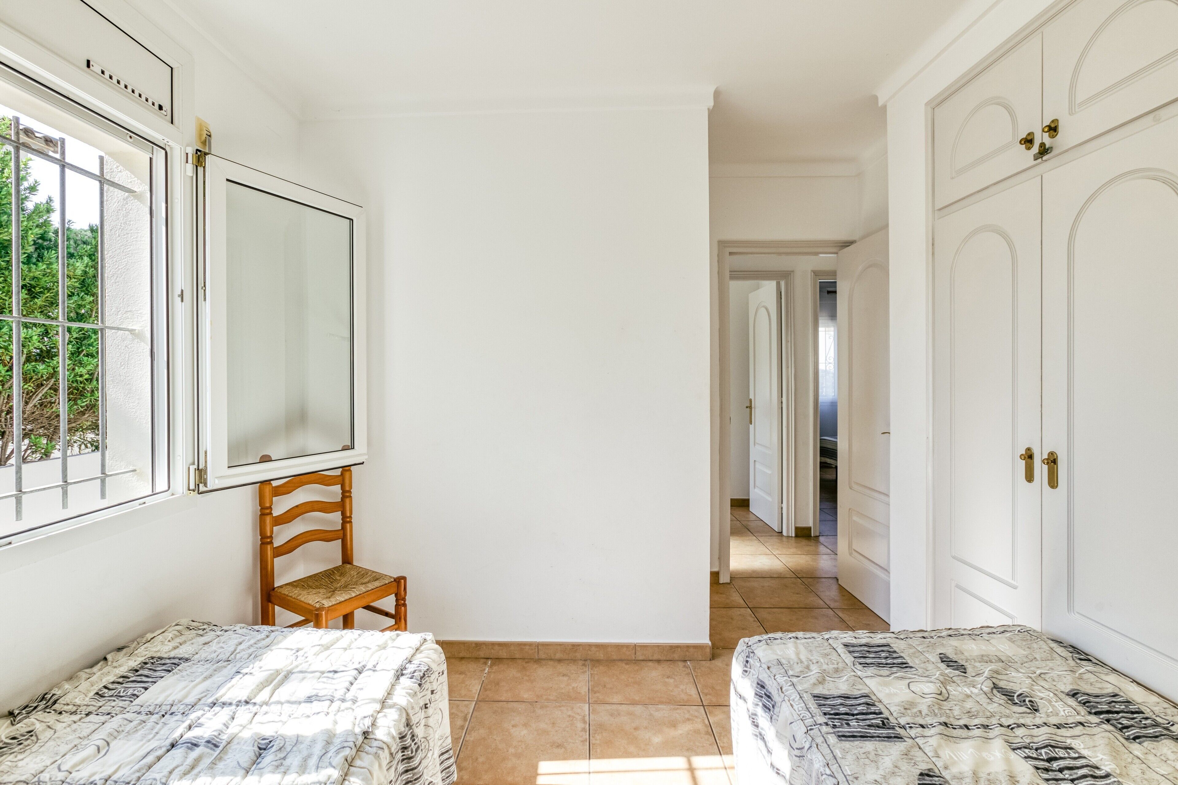 A bedroom with two beds, a wooden chair, a large mirror, and a wardrobe.
