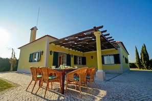 Una casa amarilla con un porche cubierto, una chimenea y un camino de entrada adoquinado.