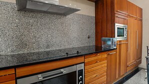 Une cuisine dotée de plans de travail en granit, de meubles en bois, d’une hotte de cuisine Bosch, d’un four à micro-ondes et d’un four Electrolux.