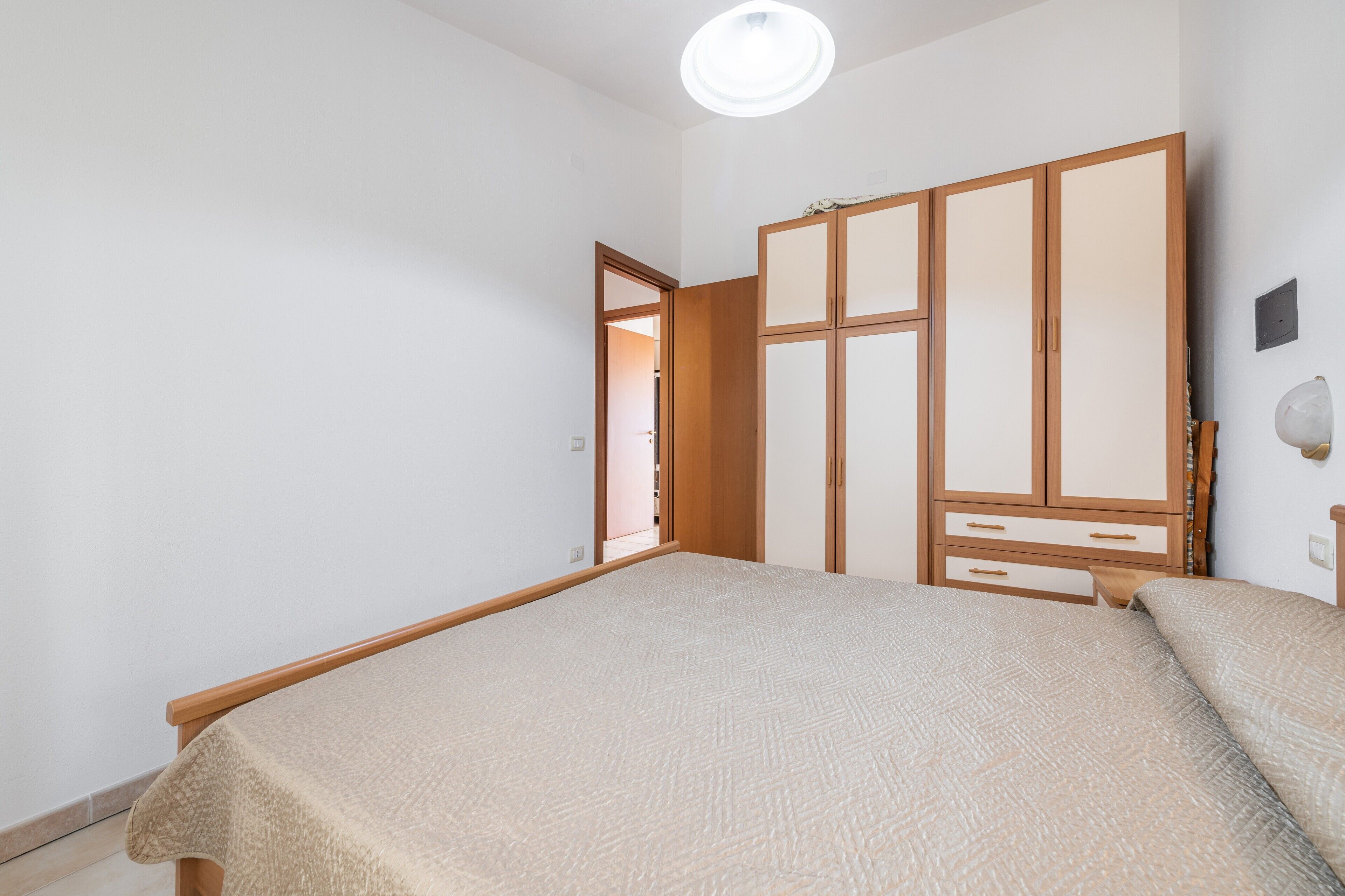 A bedroom with a bed, wooden wardrobe, and a door leading to another room.