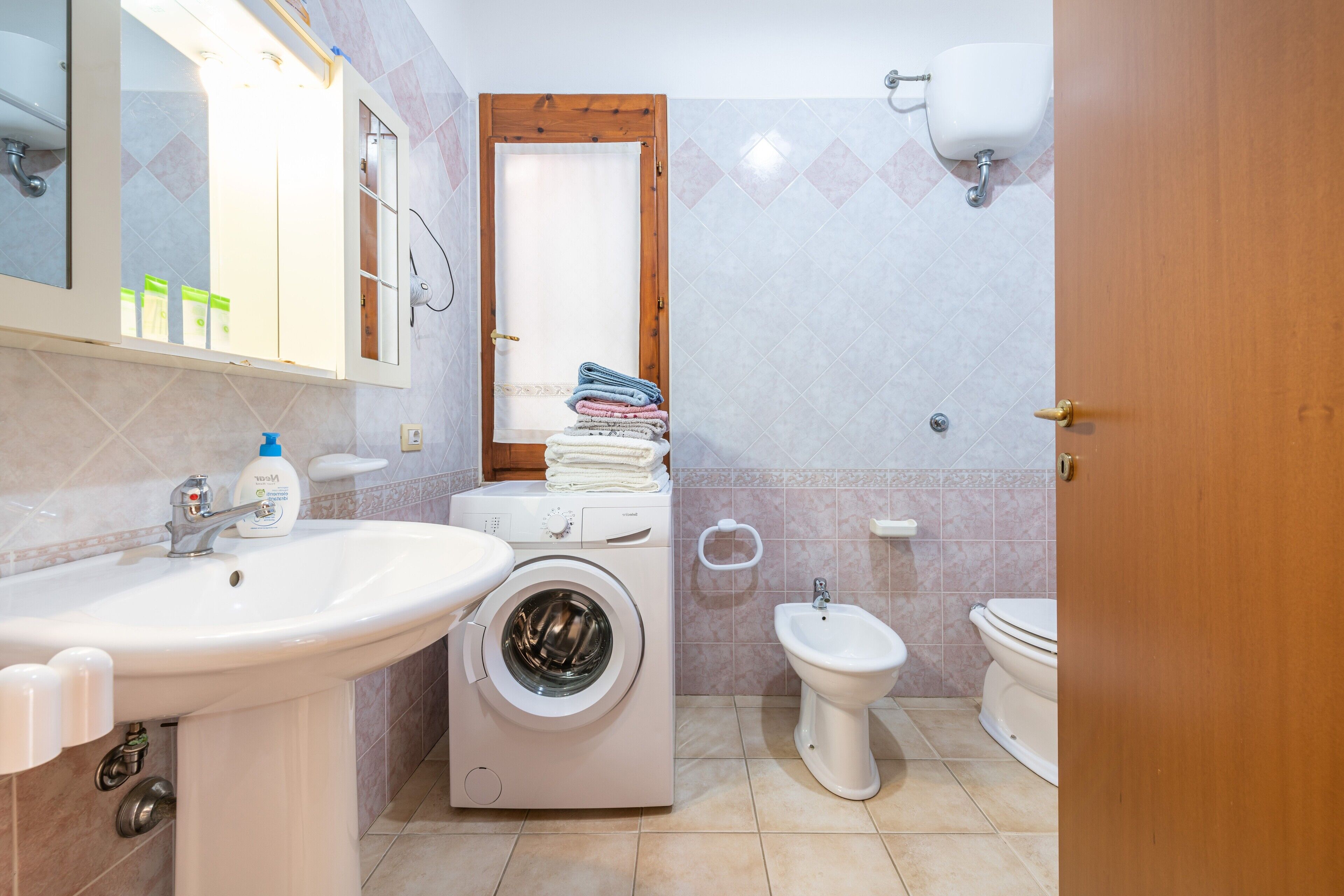 Une salle de bain équipée d’un lavabo, d’un lave-linge, d’un bidet, de toilettes et d’un miroir.