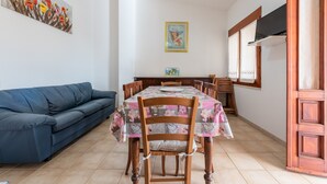 A dining area with a table set for four, a blue sofa, wooden chairs, and a painting on the wall.