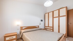 A bedroom with a bed, nightstand, wardrobe, and wall-mounted light.