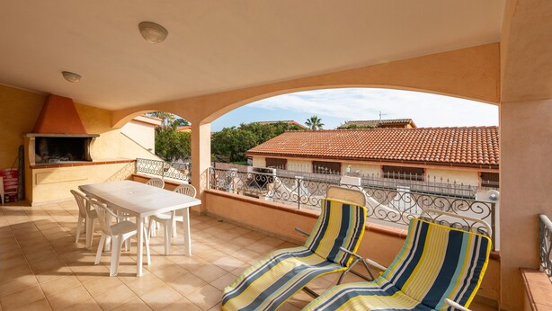 A balcony with a table and chairs, a grill, and striped lounge chairs.