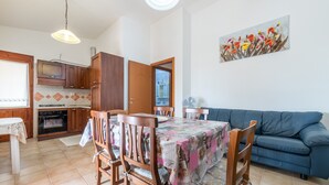 A dining area with a table set for four, wooden chairs, a blue sofa, and a kitchen in the background.