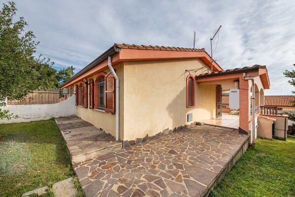Una casa con un patio de piedra, un jardín pequeño y un techo de tejas.