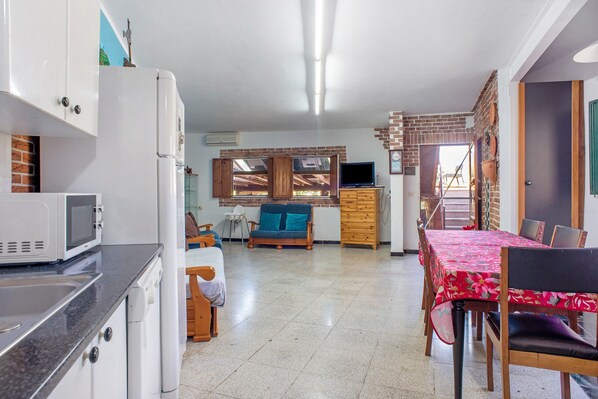 Una cocina equipada con microondas, refrigerador y lavabo. Hay una zona de comedor con mesa y sillas, y una sala de estar con sofá y televisor.