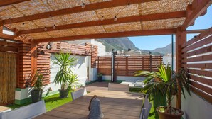 Una veranda riparata con pavimento in legno, piante in vaso e vista su una montagna.