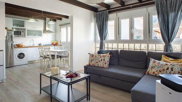 Un soggiorno moderno con divano, tavolino in vetro, zona pranzo e cucina completa di lavatrice.