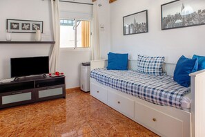 Une chambre à coucher avec un lit, une télévision, une fenêtre et un tableau représentant un paysage urbain accroché au mur.