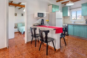 Une cuisine de taille réduite avec un plan de travail rouge, deux chaises noires, un four à micro-ondes et une cuisinière.