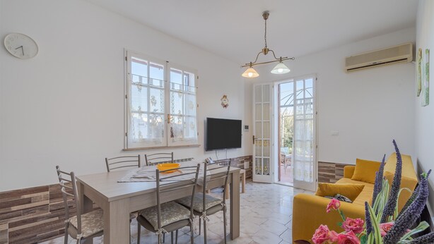 A dining area with a wooden table and chairs, a television, and a sofa with a view to the outside. - "Villa Angela" with Terrace, Shared Garden & Wi-Fi (Augusta)
