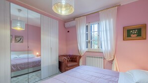 A bedroom with a bed, a chair, a window with curtains, a mirror, and a hanging light fixture. - "Villa Angela" with Terrace, Shared Garden & Wi-Fi (Augusta)