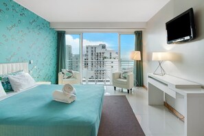 Ein Hotelzimmer mit Bett, Schreibtisch, Fernseher und einem Balkon mit Blick auf die Stadt.