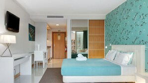 Een hotelkamer met een bed, een bureau, een stoel, een televisie en een badkamer zichtbaar door een schuifdeur.