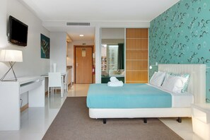 Une chambre d’hôtel équipée d’un lit, d’un bureau, d’une chaise, d’une télévision et d’une salle de bain, le tout visible à travers une porte coulissante.