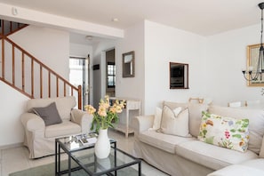 A living room with two sofas, a coffee table, a vase with flowers, a staircase, and a mirror.