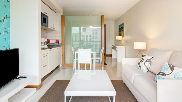 Een moderne woonkamer met een flatscreen televisie, een witte bank en een eethoek met stoelen.