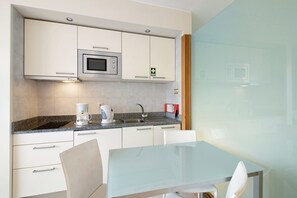 Una cuina moderna amb armaris blancs, un microones, una cafetera i una taula de vidre.