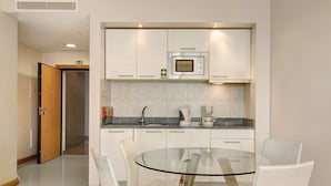 Een moderne keuken met witte kastjes, een eettafel met glazen blad en een ingebouwde magnetron.