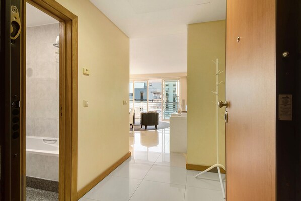 A hotel hallway with a view to a balcony, a seating area, and a door leading to a bathroom.