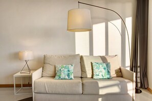 A modern living room with a sofa, two patterned pillows, a floor lamp, and a table lamp.